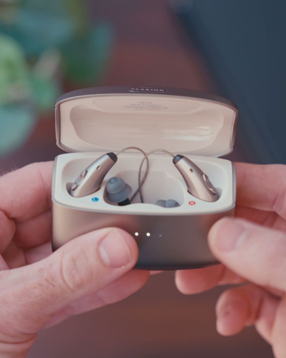 Hands holding the open Clarion charging case with both hearing aids sitting in it